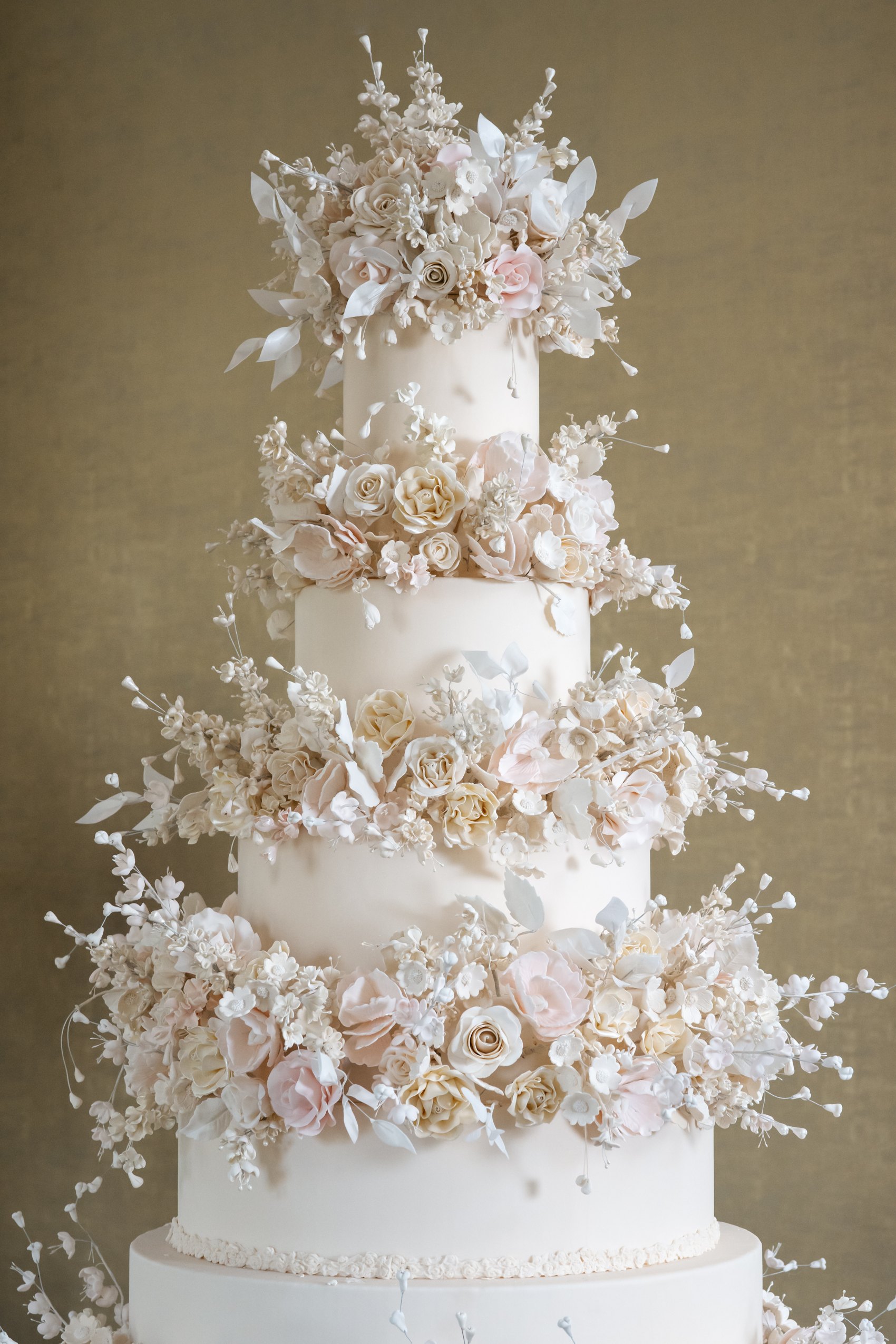 A tiered white wedding cake with sugar flower garlands on a velvet stand