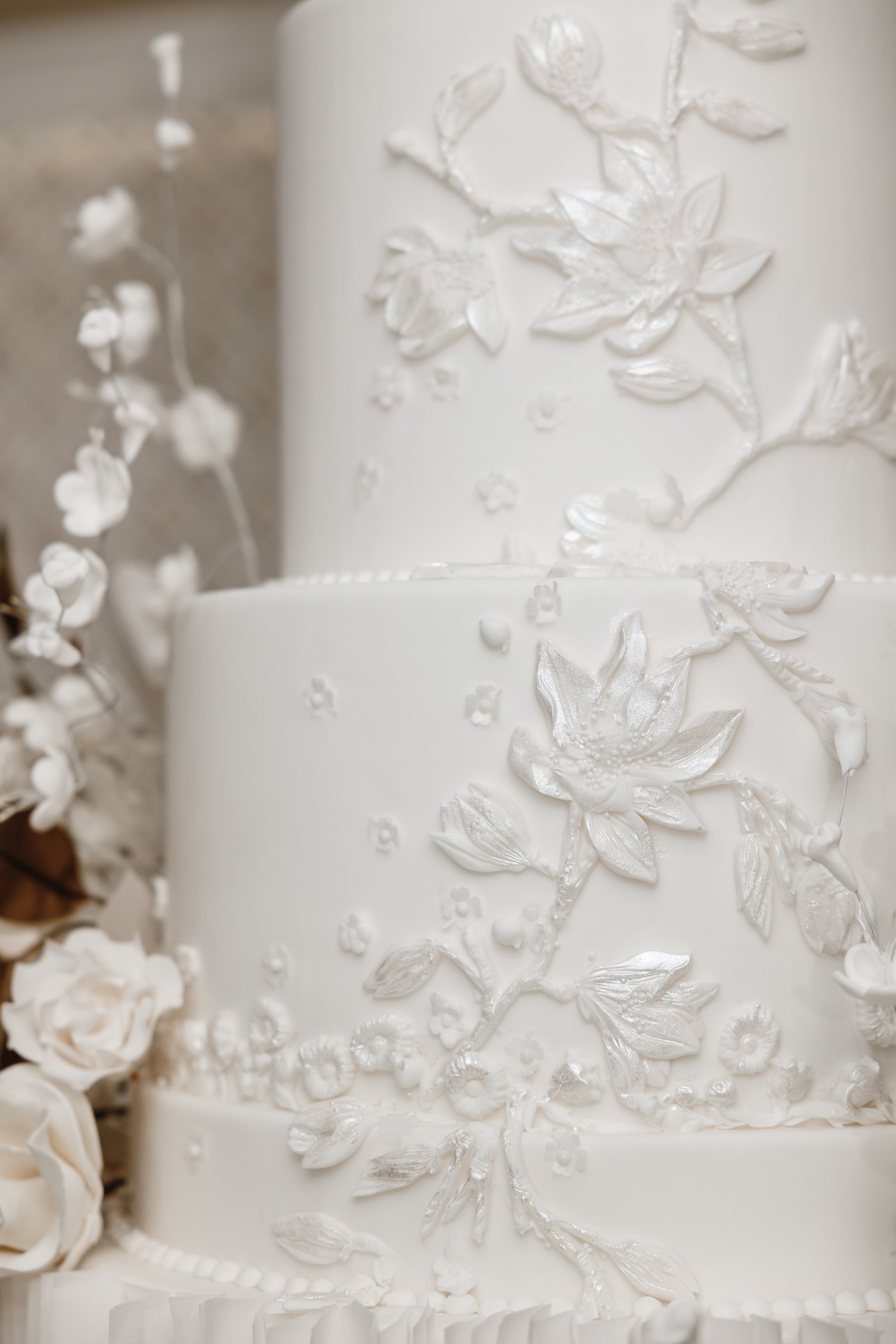 Close-up of hand-piped floral relief and sugar blossoms on a white wedding cake