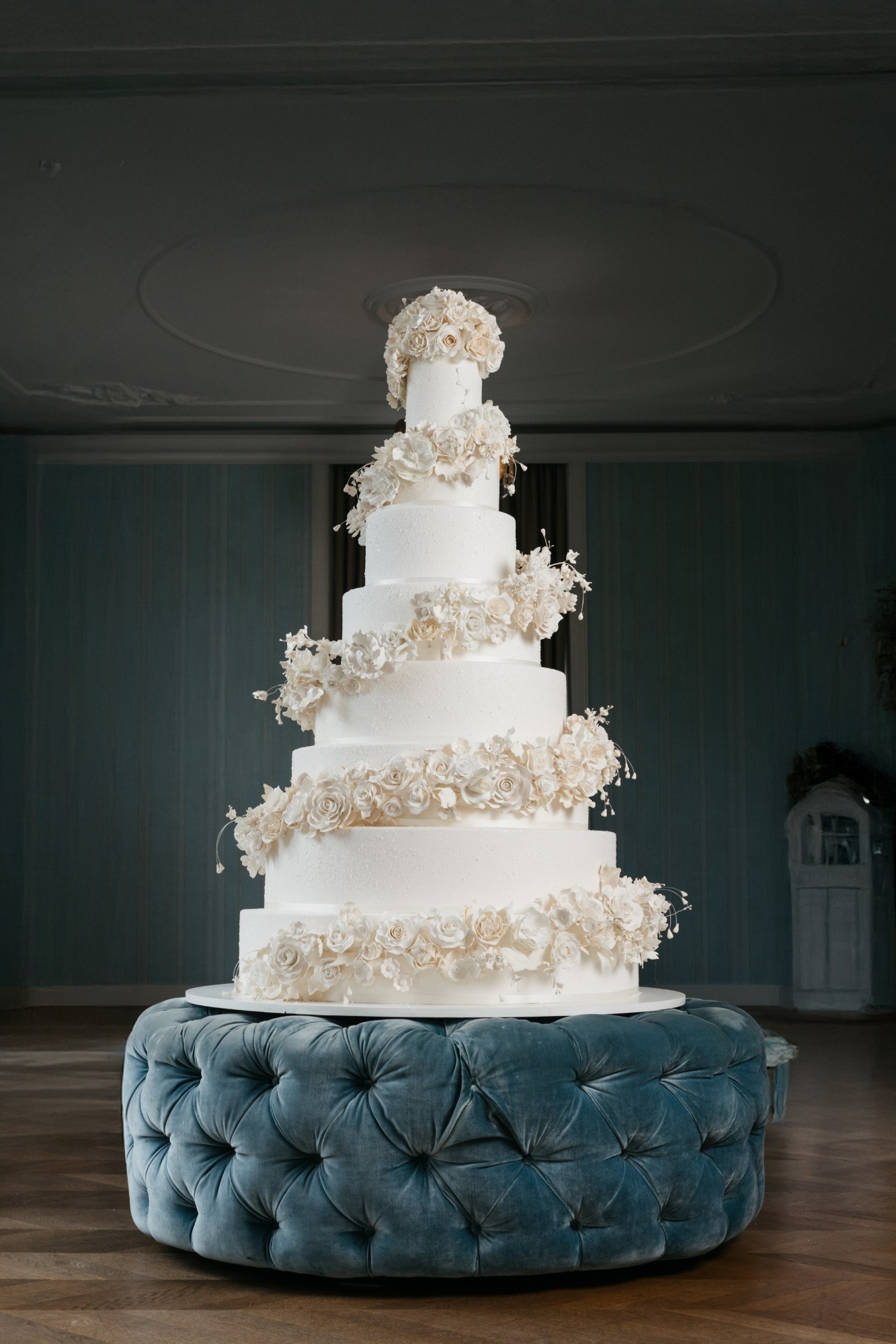 An eight-tier white wedding cake with spiralling garlands of ivory sugar roses on a velvet ottoman