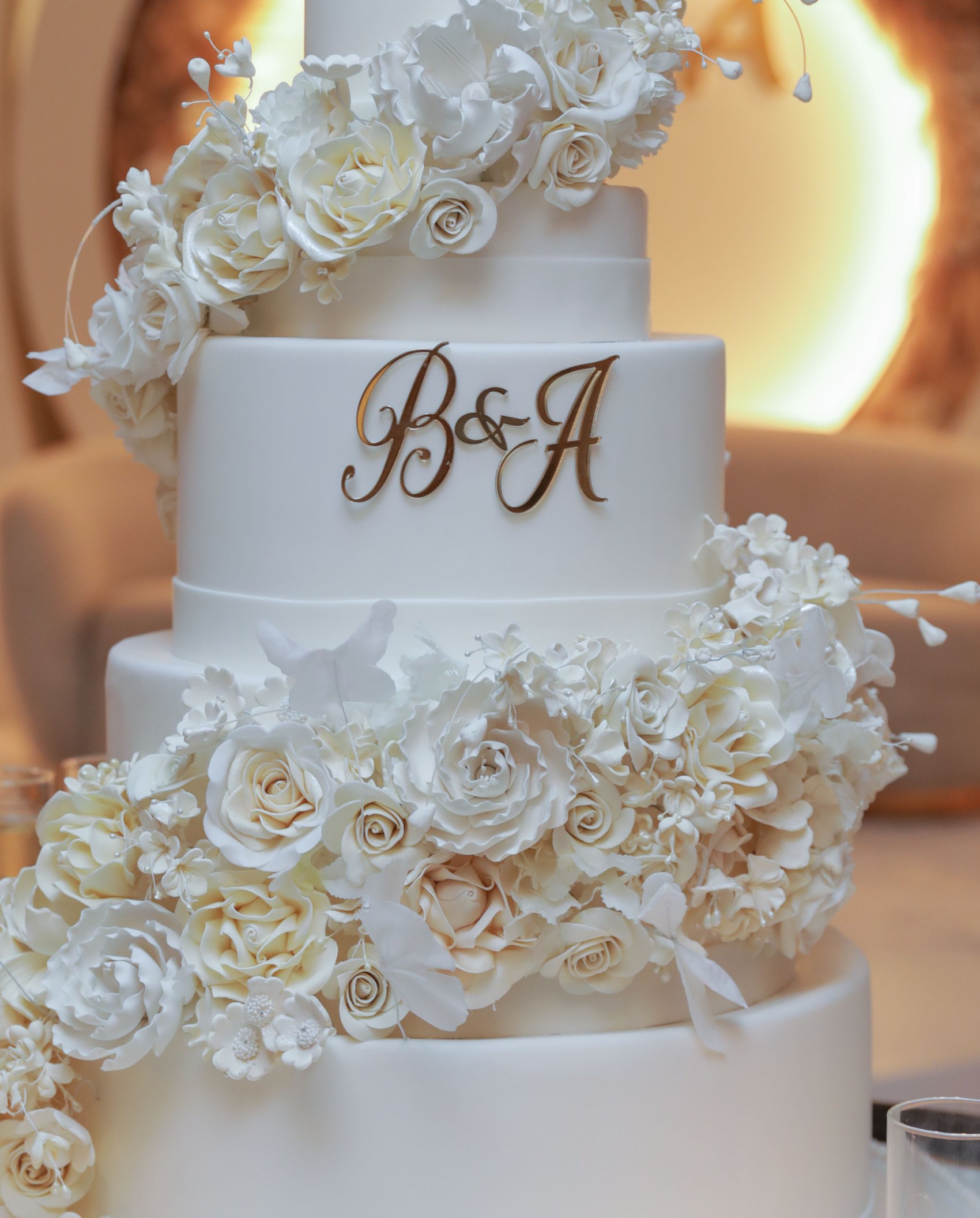 Gold initials on a white wedding cake tier with ivory sugar flowers
