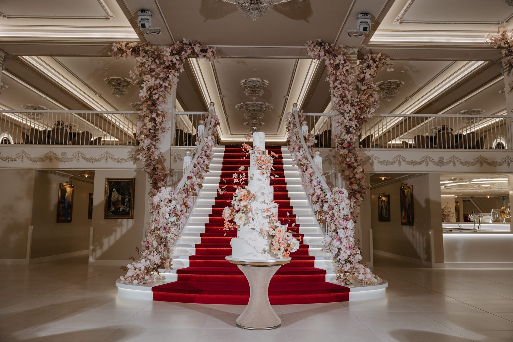A grand marble staircase with a red carpet and floral columns